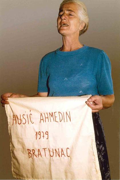 During a pre-commemoration meeting, a woman holds the square she embroidered with the name and birth year of her son, whose fate was then unknown.